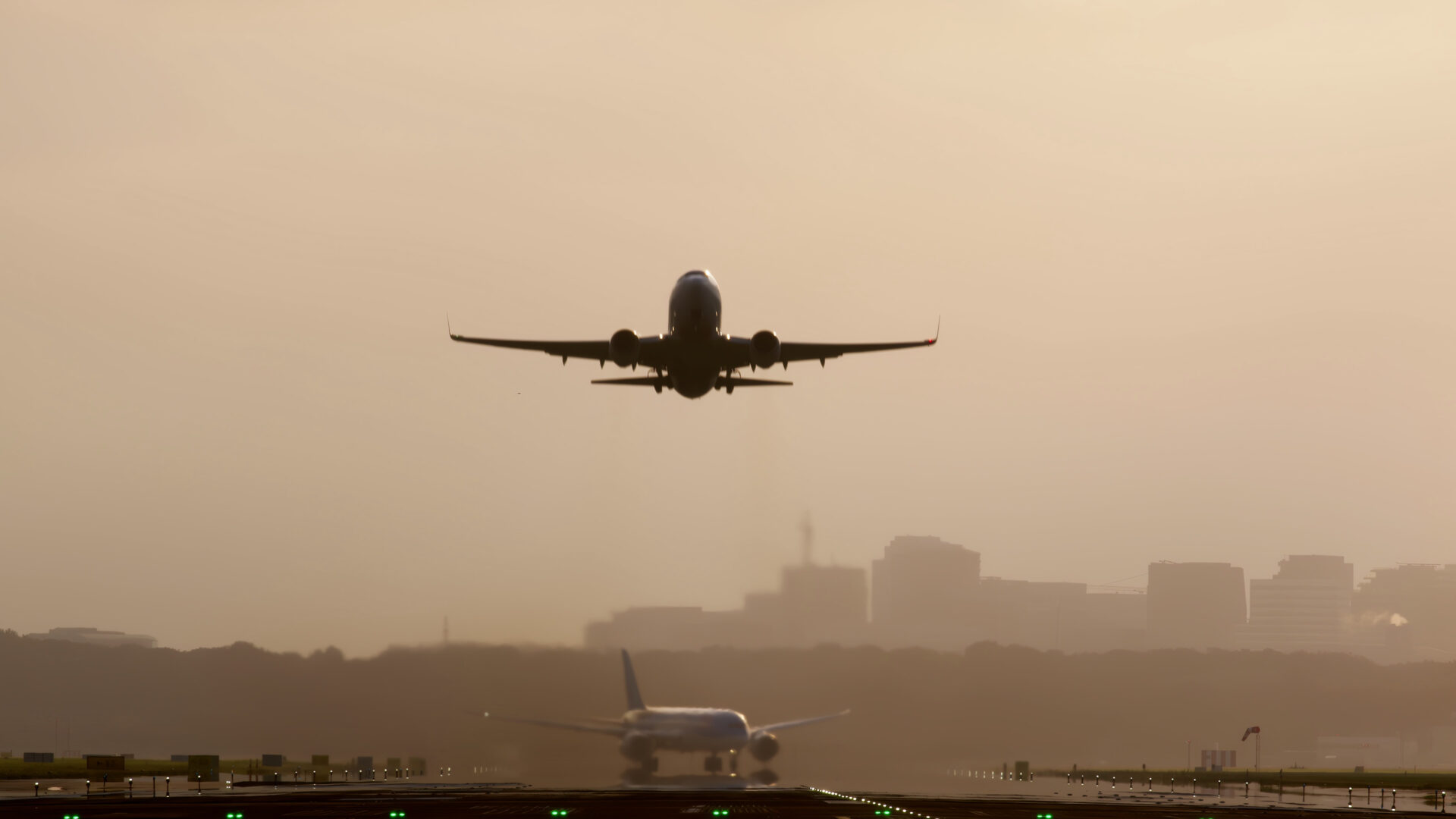 Commercial airplane taking off at sunset with another aircraft taxiing on the runway, set against a city skyline in the background.