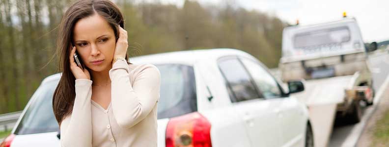 A woman making a phone call on the side of a road outside of a vehicle