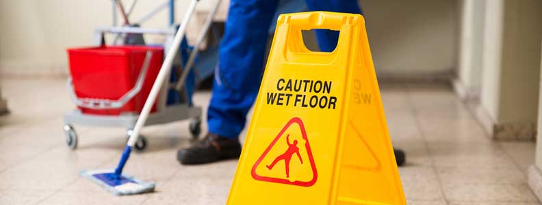 Janitor mopping floor in the background behind a wet floor sign