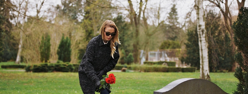 Woman laying a red rose down on a grave in a cementary