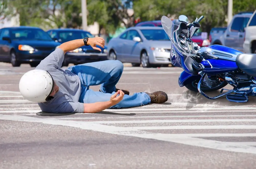 A motorcyclist lying on a Florida road after a crash with a damaged blue motorcycle nearby, surrounded by cars, emphasizing the need for immediate action