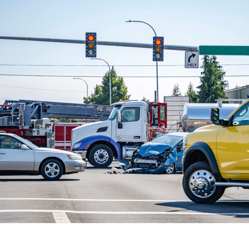 A severe truck accident at a busy intersection, showing a heavily damaged blue sedan after colliding with a semi-truck and other vehicles under a red traffic light.