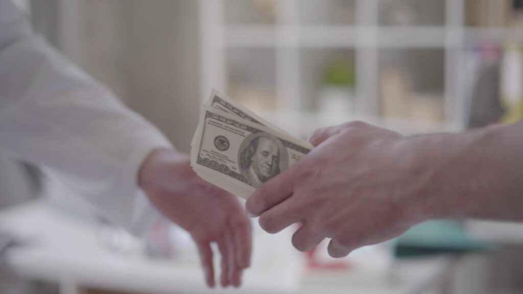 Close-up of two hands exchanging a stack of hundred-dollar bills, symbolizing financial compensation.