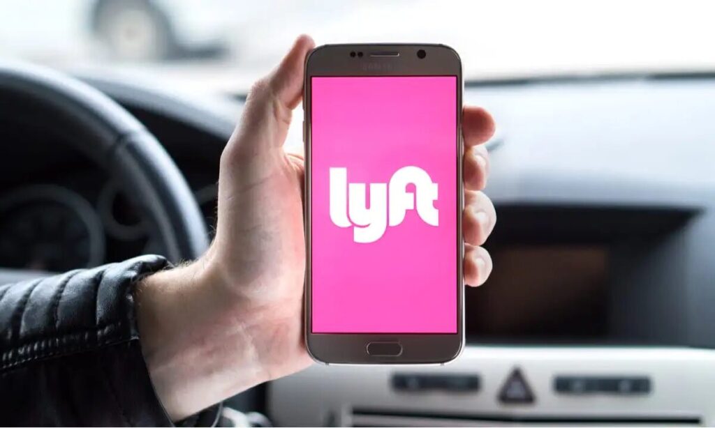 Person holding a smartphone displaying the Lyft app inside a car.