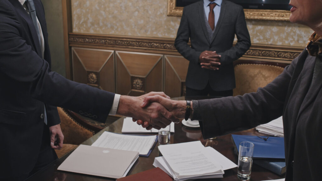 Lawyers in suits shaking hands over a table with legal documents in a Florida law office, representing a successful personal injury case settlement.