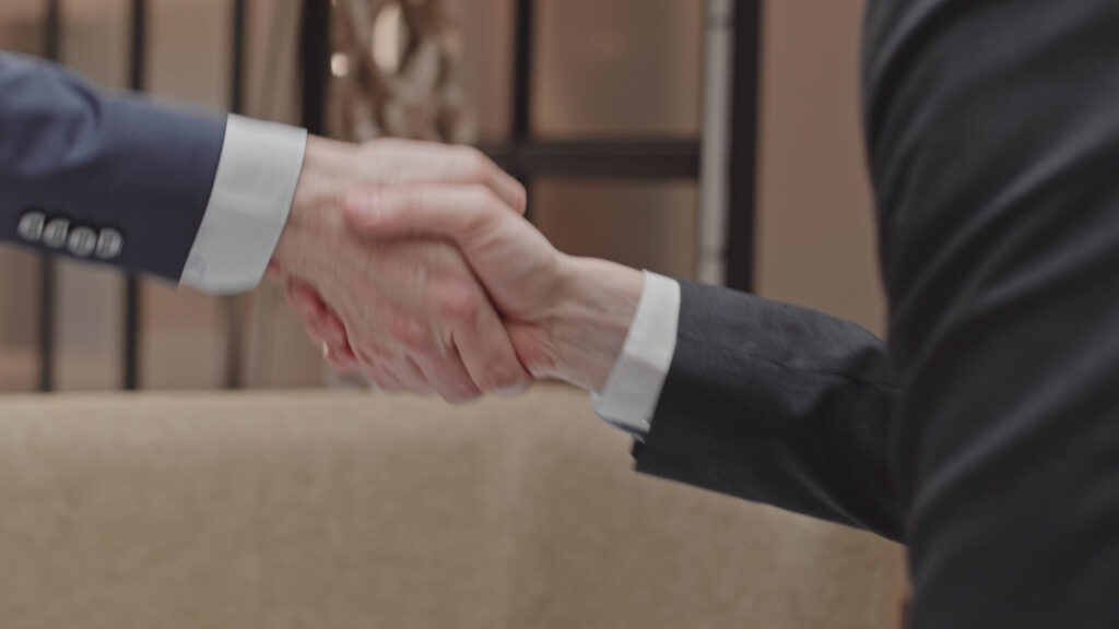 Two professionals in suits shaking hands in a refined office environment.