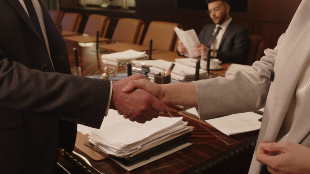 Shaking hands in a professional law office after a successful legal settlement, with documents and legal files on the desk.