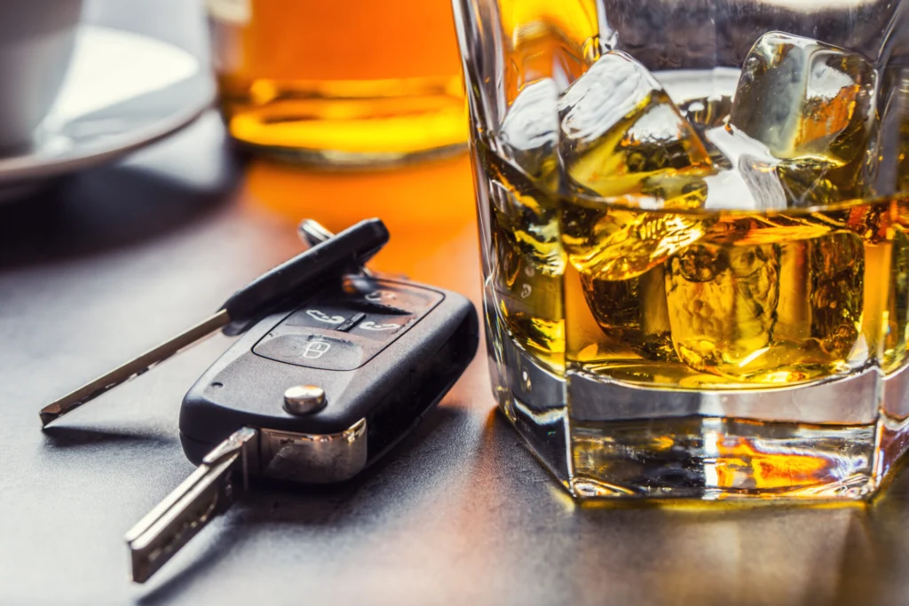 Car keys next to a glass of whiskey on a table, symbolizing drunk driving risks