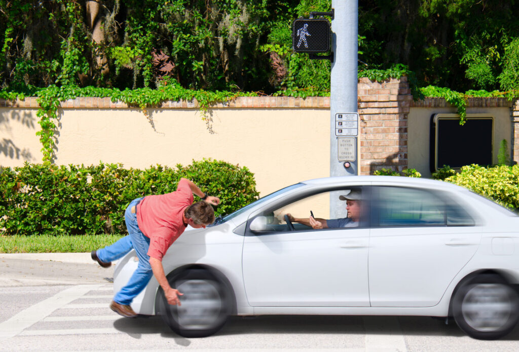 A pedestrian in a red shirt is struck by a white car at a crosswalk, with the driver holding a phone.