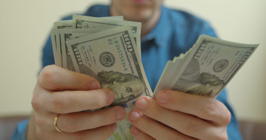 Hands holding stacks of $100 bills, symbolizing compensation for Florida motorcycle accident victims