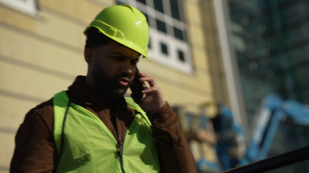 Concerned construction worker in green hard hat and vest calling for legal help after accident at Florida job site