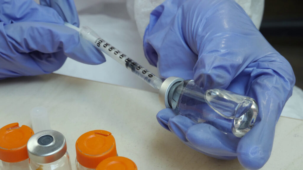 Gloved medical professional drawing vaccine into a syringe from a vial, illustrating rabies post-exposure prophylaxis preparation.