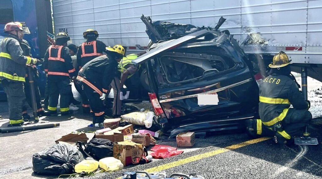 Firefighters from St. Lucie County Fire District rescue trapped victims from a crushed black SUV under a jackknifed semi-truck trailer on Florida Turnpike in Fort Pierce, with debris scattered on the road.