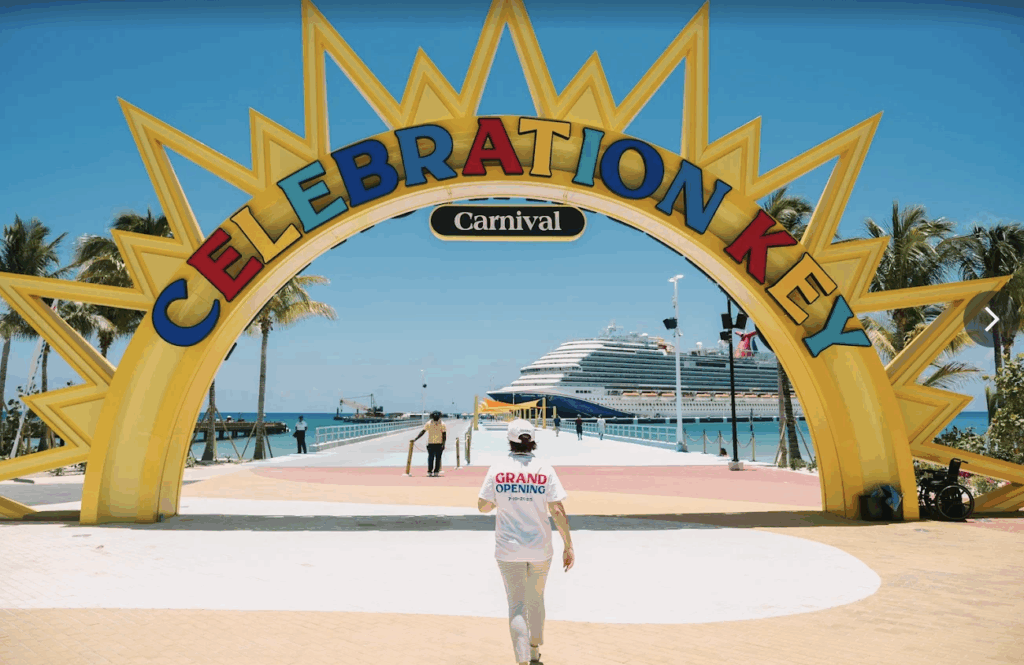 Vibrant entrance arch at Carnival's Celebration Key resort in the Bahamas, featuring a colorful sun-shaped sign with a docked cruise ship and visitors walking on a sunny pier during grand opening.