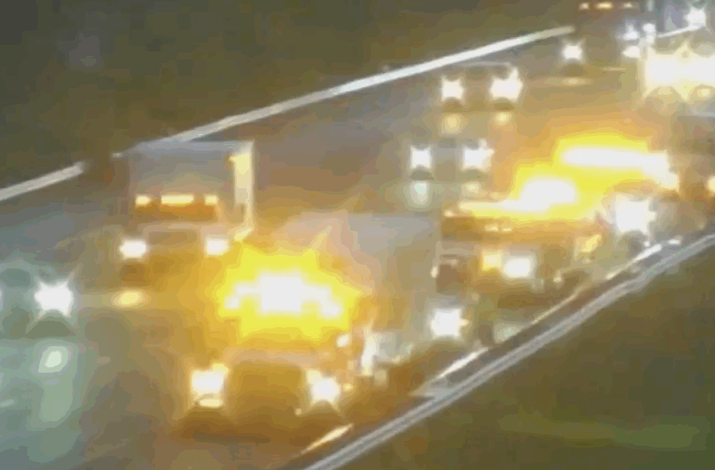 A nighttime highway scene with multiple vehicles involved in a crash, including a semi-truck, with bright emergency lights illuminating the wreckage on I-4 in Volusia County.