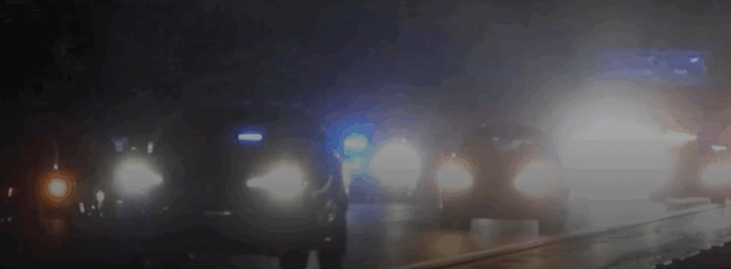 A nighttime scene of a highway crash with emergency lights from police and rescue vehicles illuminating the area, showing multiple cars and a wet road.