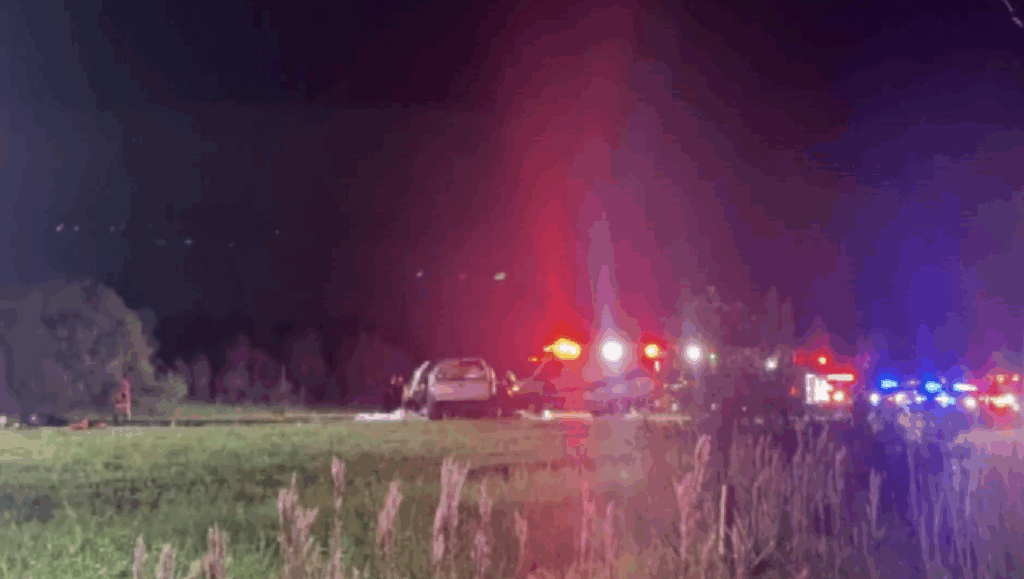 Emergency vehicles with flashing lights at a nighttime car accident scene on Burnt Store Road, Cape Coral, with a crashed SUV and police activity.