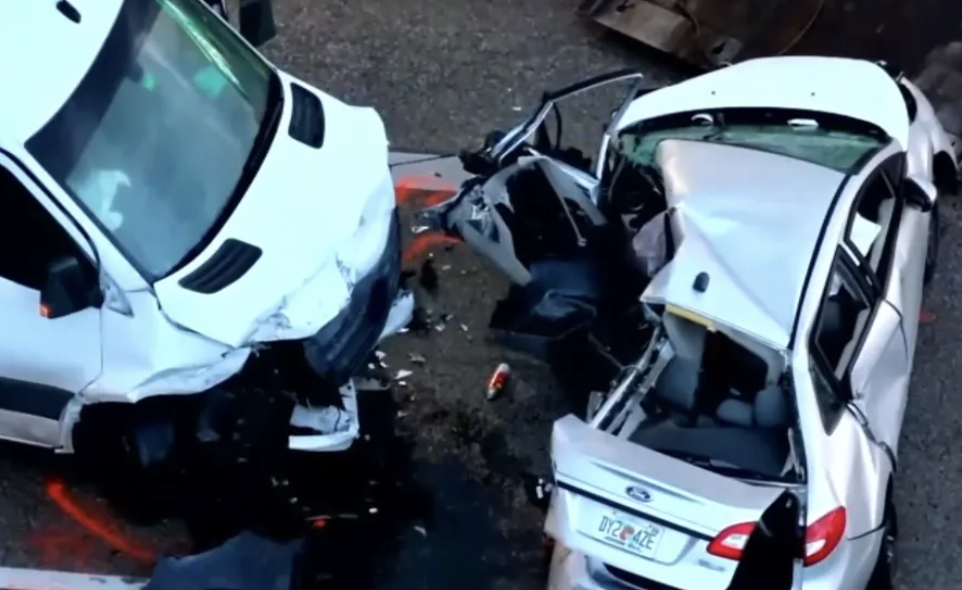 Damaged white van and sedan after a severe car crash on a highway, with debris scattered around.