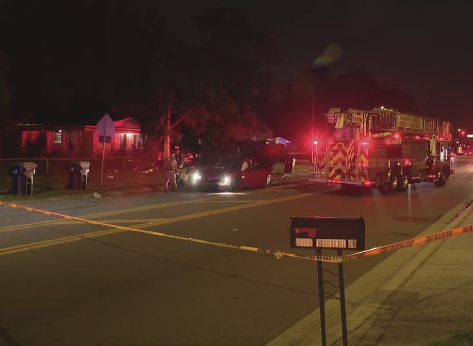 Nighttime scene of a car crash with emergency vehicles and police tape on a residential street.