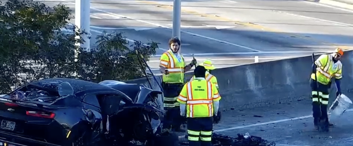 Damaged black Chevrolet Camaro after wrong-way head-on crash on I-95 in Miami Gardens, with FDOT cleanup crew and debris scattered across the highway.