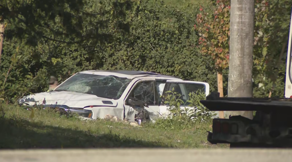 White pickup truck with shattered windshield and severe front-end damage resting in a grassy ditch after an Oakland Park car accident.