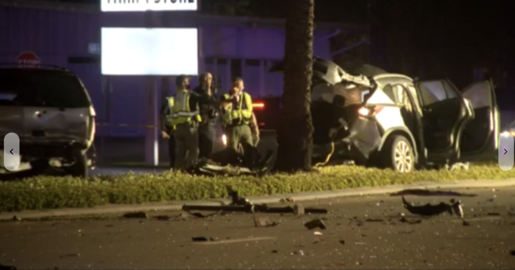 Nighttime car accident scene in Largo with police officers investigating, two damaged vehicles including a sedan against a tree, and debris on the road.