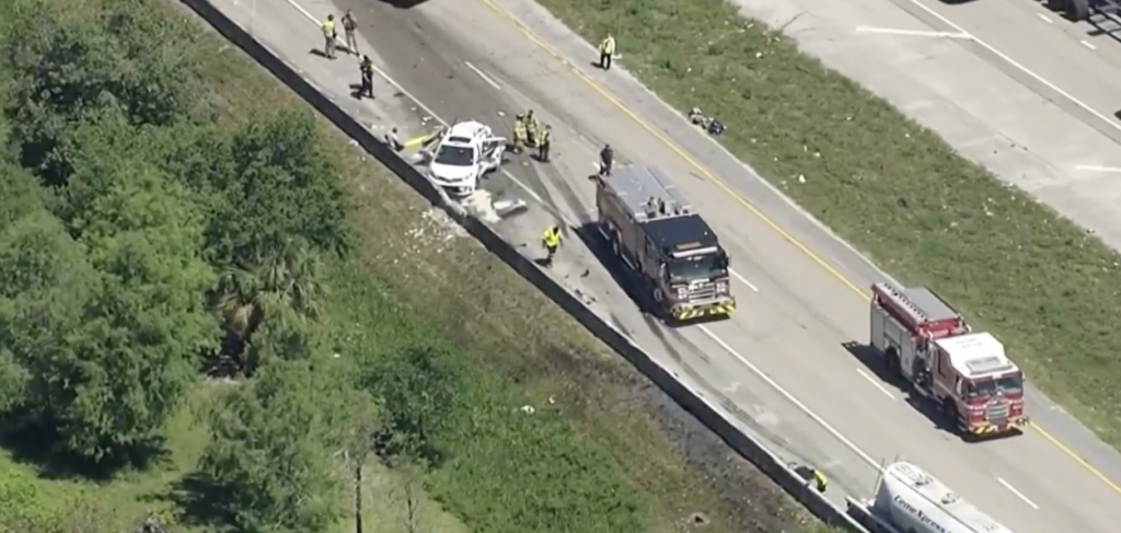 Aerial view of the I-595 to I-95 ramp crash scene in Fort Lauderdale with a cement truck, damaged taxi, and emergency responders